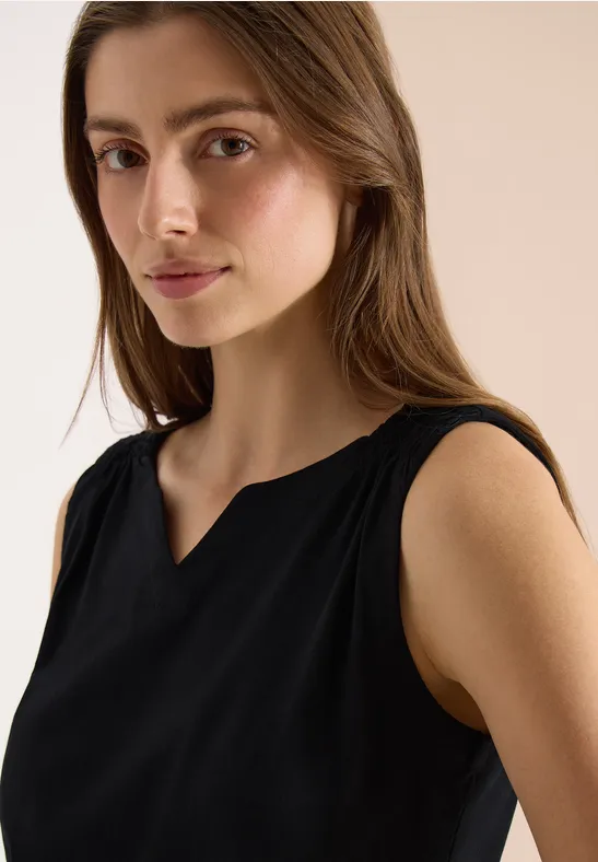 Une personne porte un haut sans manches noir devant un fond clair.