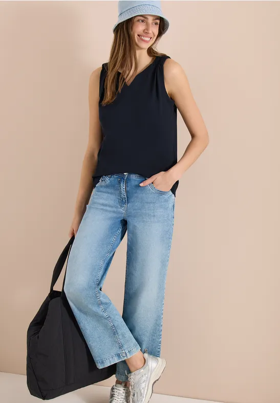 Frau trägt weite Jeans, dunkelblaues Top, weiße Sneaker, hellblaue Cap und schwarze Tasche.