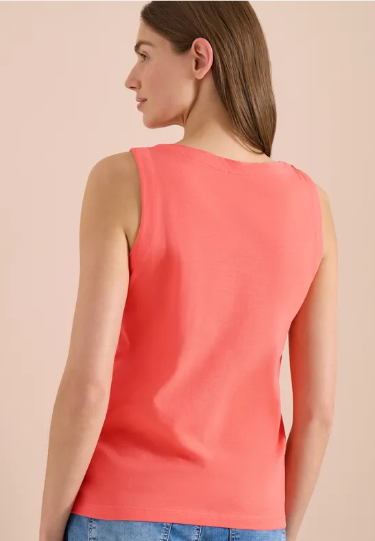 Eine Frau von hinten trägt ein korallenfarbenes ärmelloses Top.