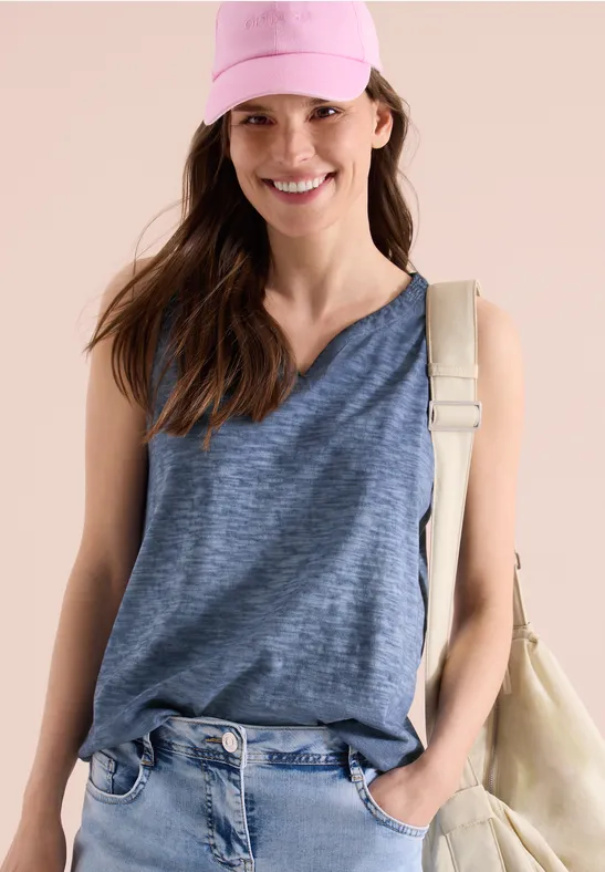 Frau in legerem blauen Top, Jeans, rosa Cap und Schultertasche.