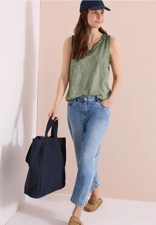 Frau in grünem Tanktop, Jeans und Cap trägt große schwarze Tasche und beige Schuhe.