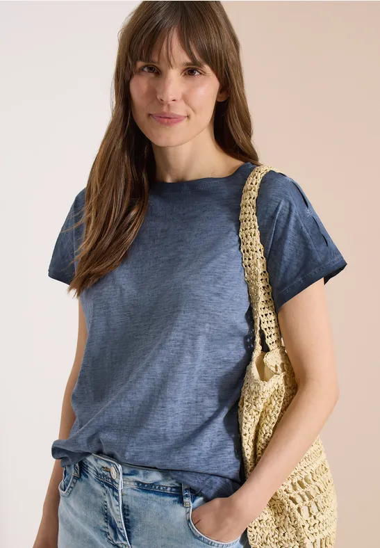 Frau mit unkenntlich gemachtem Gesicht, trägt blaues T-Shirt, Jeans und geflochtene Strohtasche.