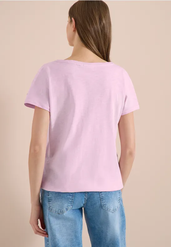 Femme de dos portant un T-shirt rose clair à manches courtes et un jean bleu sur fond neutre.