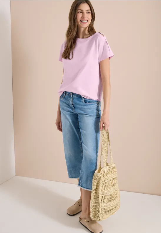 Une femme porte un t-shirt rose, un jean large, des chaussures plates et un sac en paille.