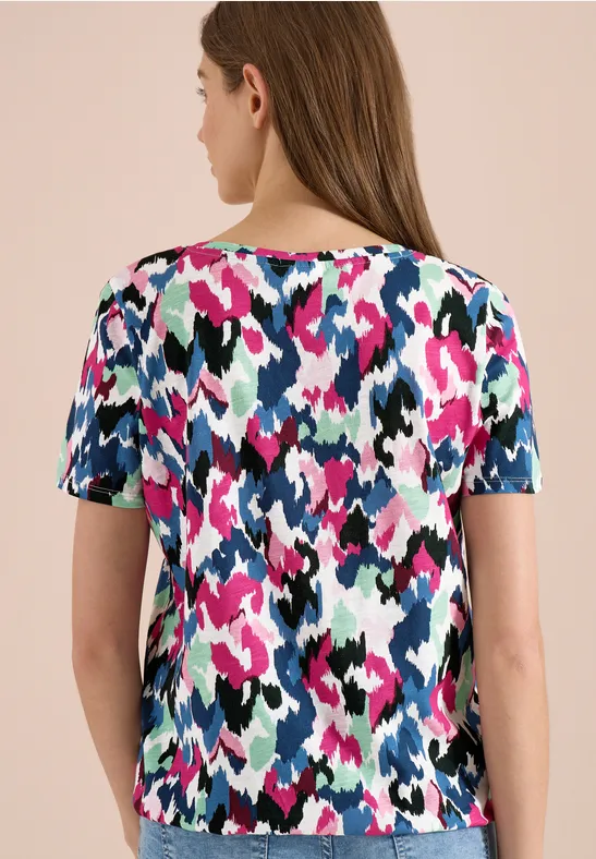 Frau von hinten in kurzärmligem T-Shirt mit abstraktem Muster in Pink, Blau, Weiß, Schwarz und Grün.