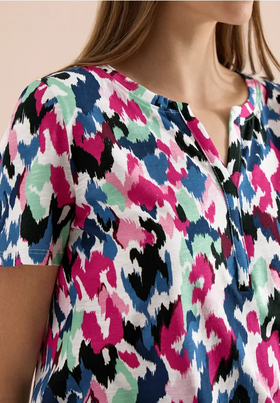 Damenbluse mit kurzärmeligem Schnitt und abstraktem, mehrfarbigem Muster in Pink, Blau, Schwarz und Weiß.