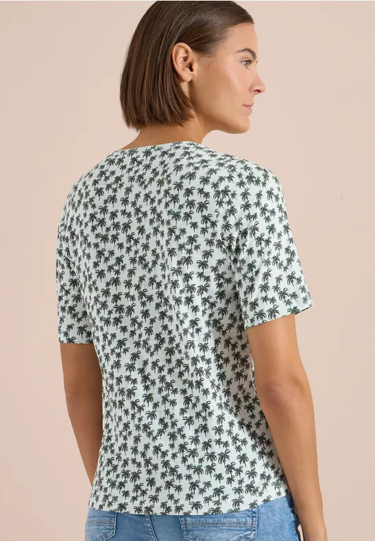 Frau von hinten in einem weißen T-Shirt mit kleinem grünen Blumenmuster.