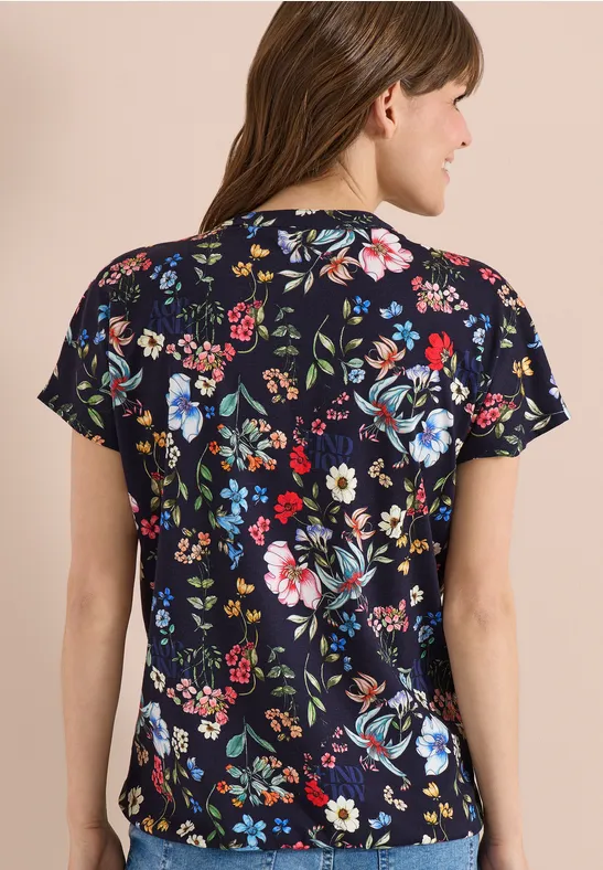 Eine Person von hinten in einem dunkelblauen T-Shirt mit buntem Blumenmuster.