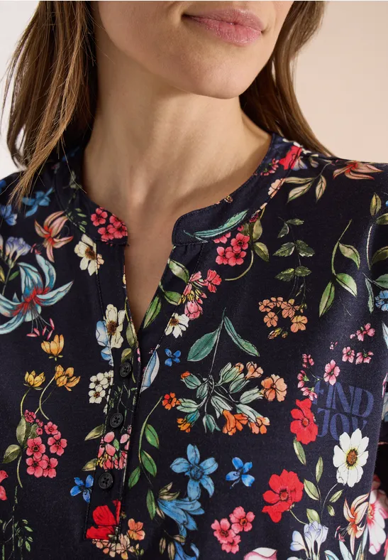 Frau trägt dunkelblaues Oberteil mit buntem Blumenmuster und Knopfleiste im Close-up.