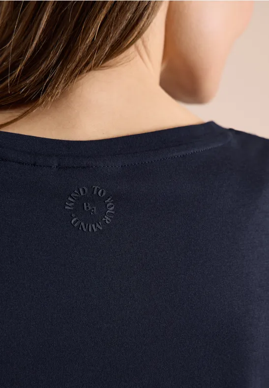 Vue de dos d'une personne portant un t-shirt bleu foncé à col rond avec petit logo imprimé.