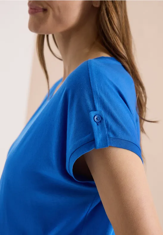 Vue de profil d'une femme portant un t-shirt bleu à manches courtes avec un bouton.