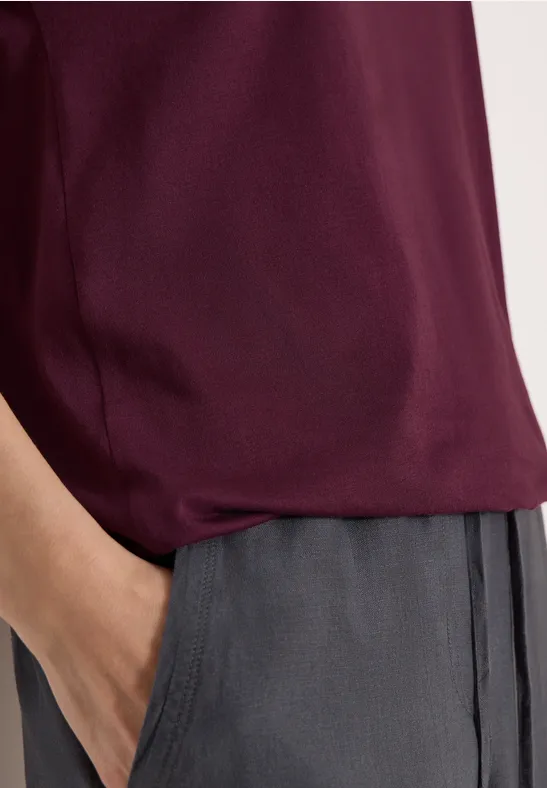 Haut bordeaux, pantalon gris, une main dans la poche.