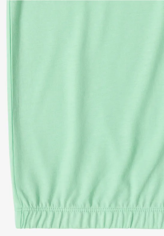 Unterer Teil eines mintgrünen Kleidungsstücks mit elastischem Saum auf weißem Hintergrund.