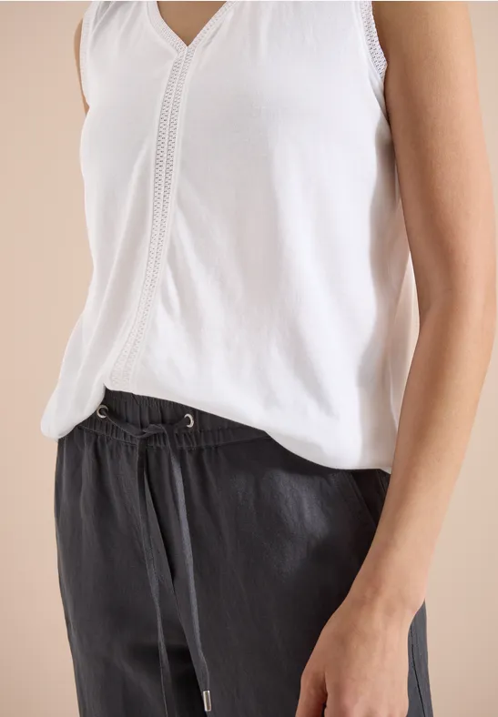 Weißes ärmelloses Top und schwarze Hose mit Tunnelzug, lässiger Stil.