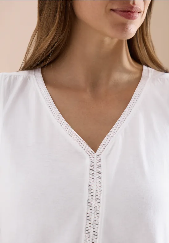 Nahaufnahme einer Frau in weißem V-Ausschnittshirt mit zierlicher Spitzenverzierung am Kragen.