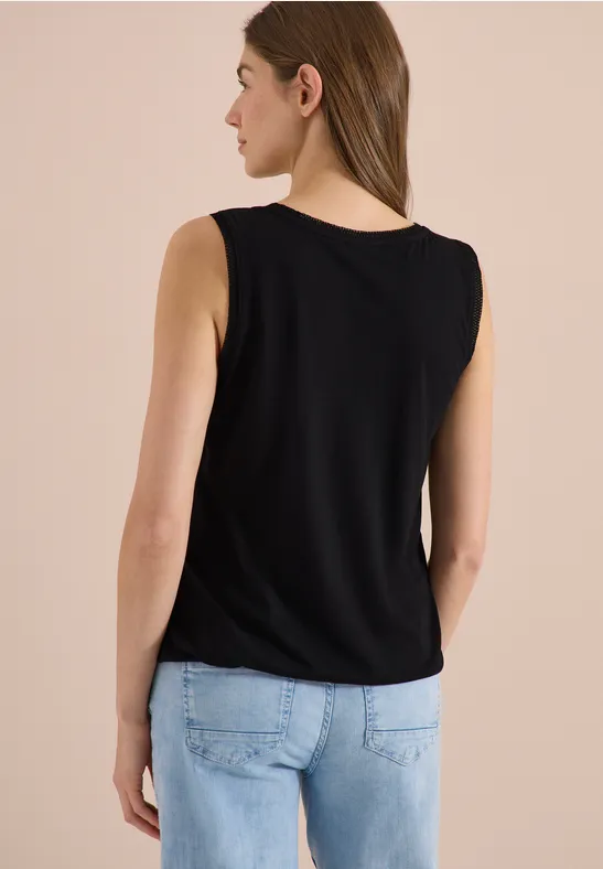 Frau von hinten in schwarzem, ärmellosem Top und hellblauen Jeans vor neutralem Hintergrund.
