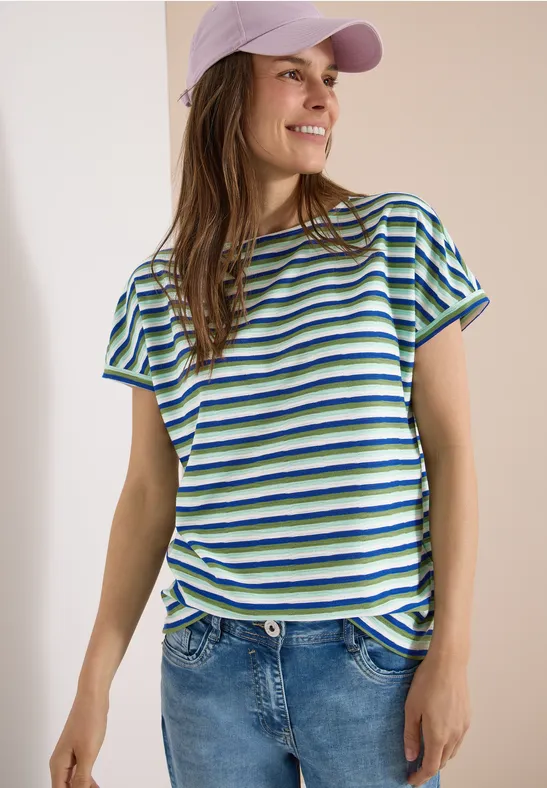 Frau in gestreiftem blau-grün-weißem T-Shirt, mit Jeans und Cap.