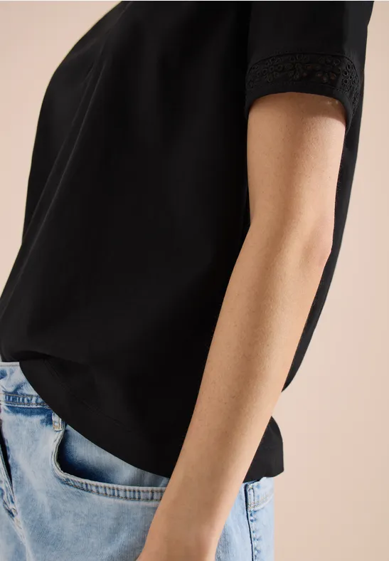 Frau in schwarzem T-Shirt und Jeans, Hand lässig in der Hosentasche.