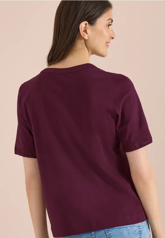 Frau von hinten in locker sitzendem, violettem T-Shirt vor hellbeigem Hintergrund.