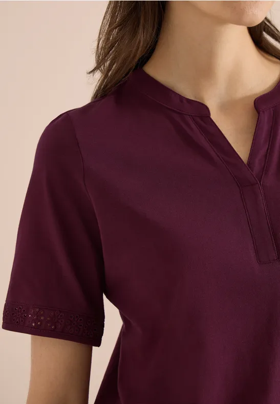 Damenoberteil in Bordeauxrot mit kurzem Ärmelansatz und V-förmigem Ausschnitt, feine Lochstickerei am Ärmelsaum.