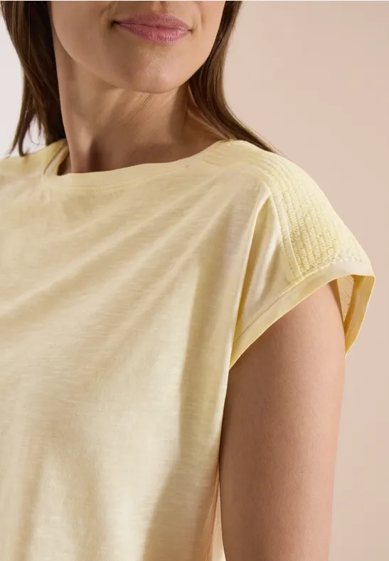 Nahaufnahme einer Frau im gelben, kurzärmligen Shirt mit rundem Halsausschnitt.