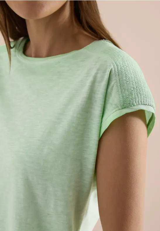 Frau in hellgrünem T-Shirt mit strukturierter Stoffpartie an den Schultern