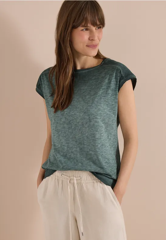 Person mit grünem T-Shirt und beiger Hose, Hände in den Taschen