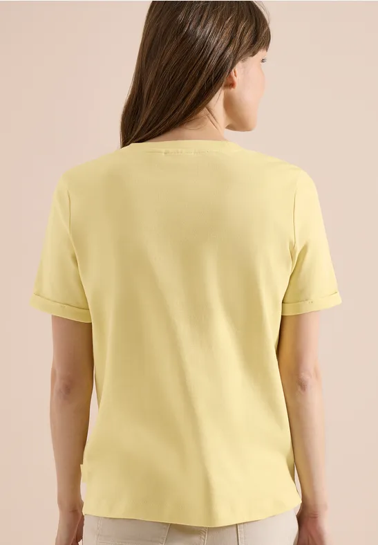Une femme de dos portant un t-shirt jaune pâle à manches courtes sur fond clair.