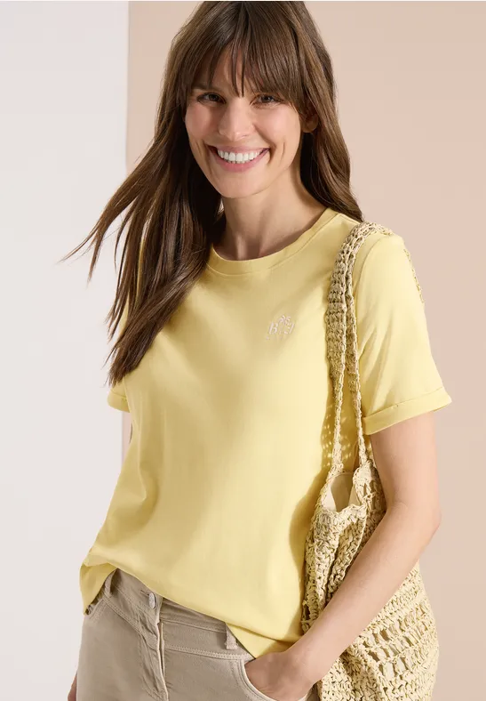 Une femme porte un t-shirt jaune pâle et un sac en maille crochetée.