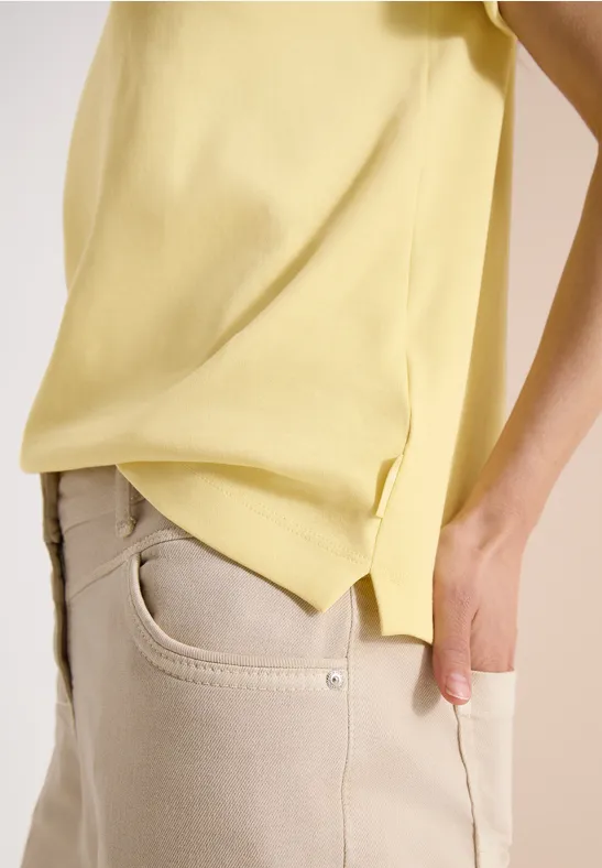 Vue de profil d'une personne en jean beige et t-shirt jaune lâche sur fond clair.