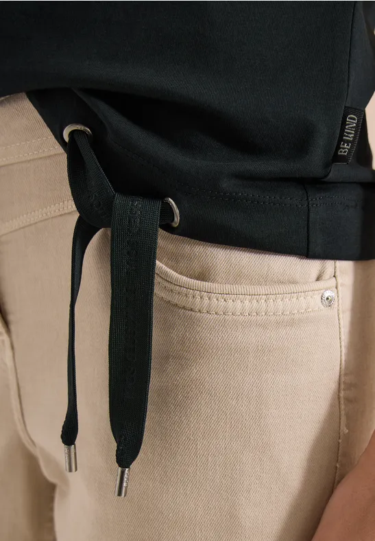 Ein schwarzer Hoodie mit lockeren Kordeln über einer beigen Jeanshose.