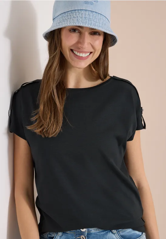 Femme portant un t-shirt noir et un bob en jean devant un mur clair.