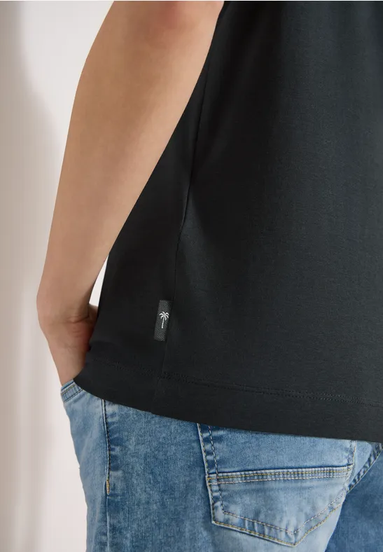 Personne de dos portant un t-shirt noir et un jean bleu, main dans la poche.