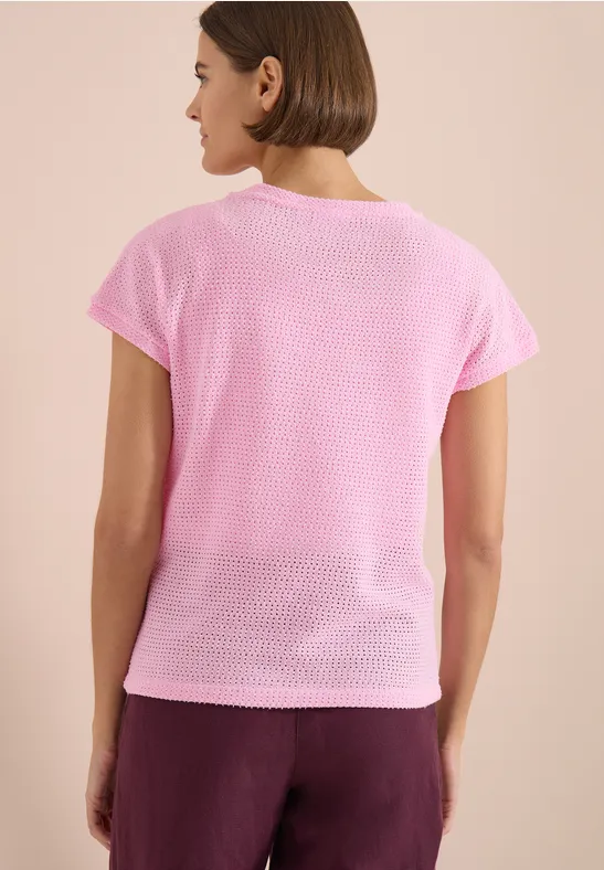 Une femme vue de dos portant un tee-shirt rose et un pantalon bordeaux sur fond clair.