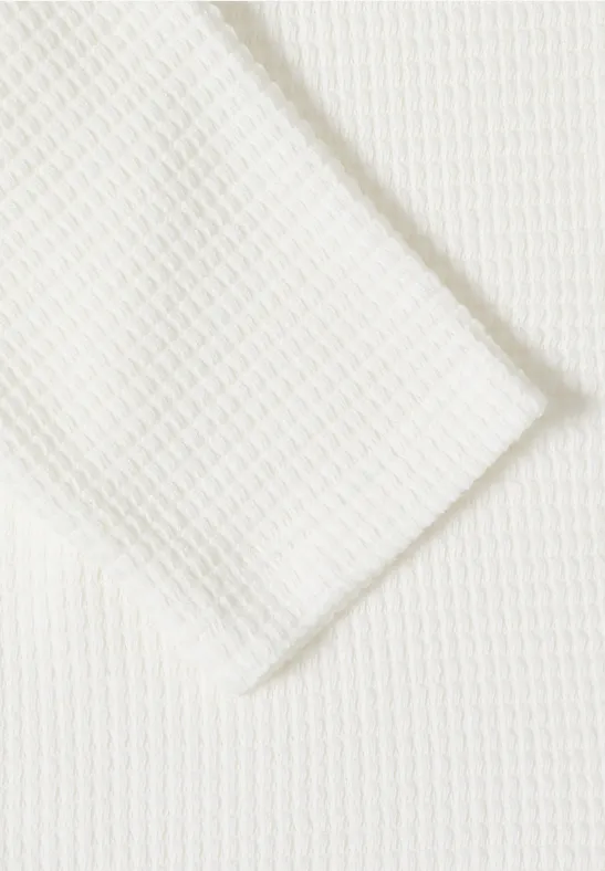 Gros plan sur un tissu blanc à structure gaufrée, motif nid d’abeille ou losanges.