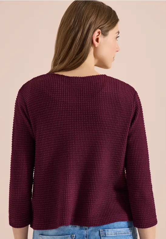 Une personne de dos portant un pull en maille violet foncé et ample.