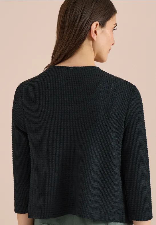 Femme de dos portant un haut en maille noire texturée à manches 3/4.