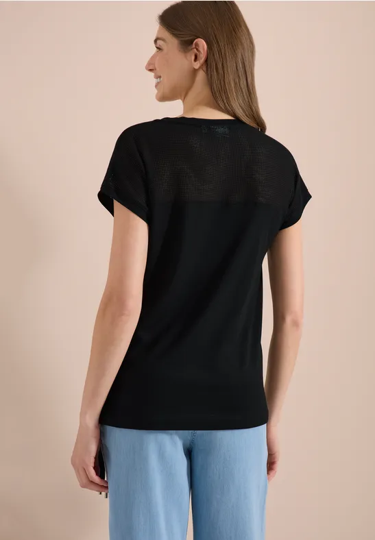 Frau von hinten in schwarzem T-Shirt und blauen Jeans vor neutralem Hintergrund.