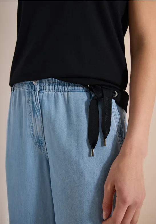Teilansicht einer Person in schwarzem Oberteil mit seitlichen Bändern und hellblauen Jeans.