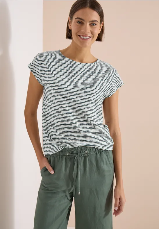 Frau trägt gestreiftes, kurzärmeliges Shirt und grüne, lässige Hose.