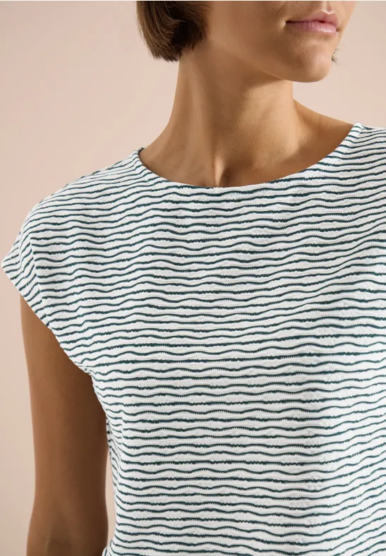 Halbkörperansicht einer Frau in schlichtem weißem T-Shirt mit feinen, schwarzen Wellenstreifen.