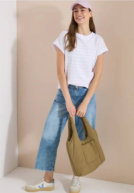 Femme en t-shirt blanc, jean large, baskets blanches, tenant un grand sac épaule matelassé kaki.