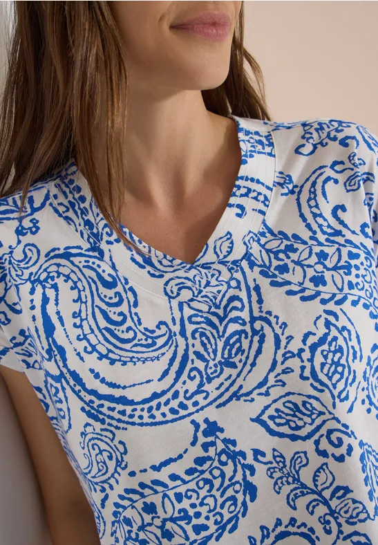 Frau trägt ein weißes Oberteil mit blauem Paisley-Muster und V-Ausschnitt.