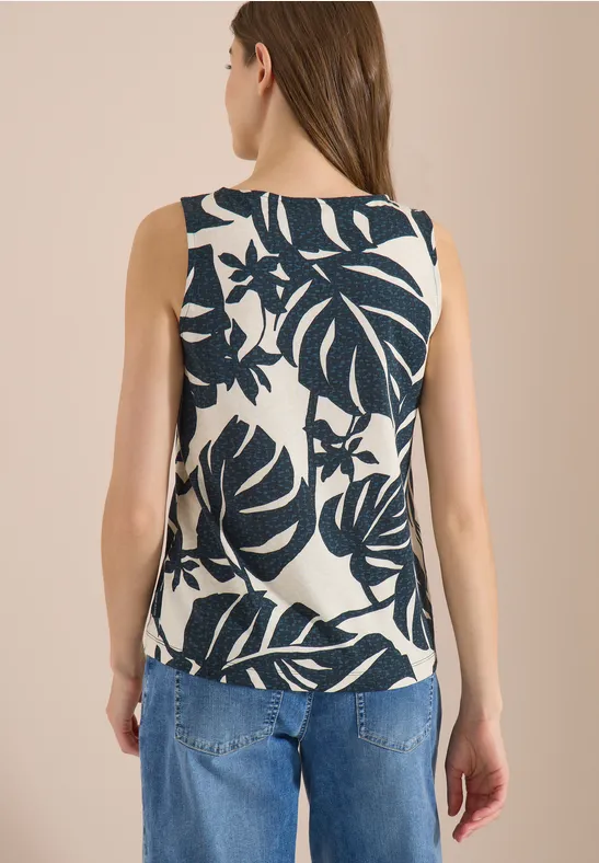 Achteraanzicht van vrouw in mouwloze top met donkerblauw bladmotief en spijkerbroek.