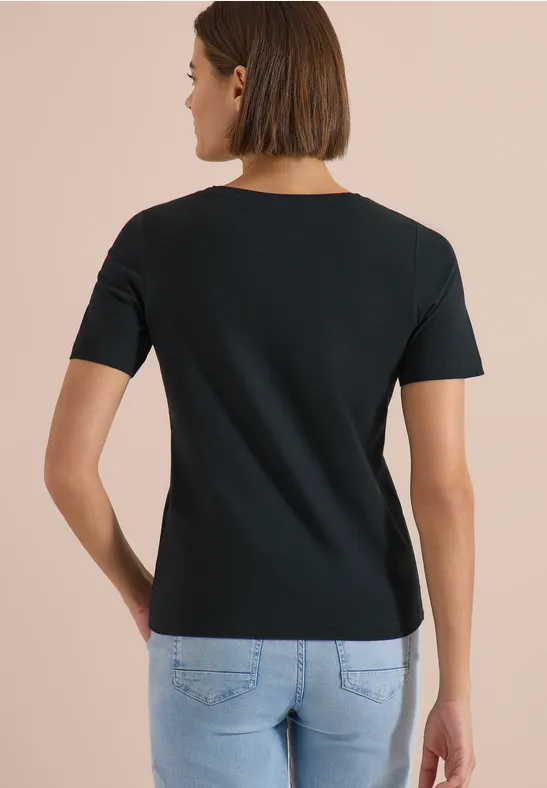 Eine von hinten gesehene Frau in schwarzem Kurzarmshirt und hellblauen Jeans vor neutralem Hintergrund.