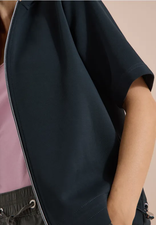Personne porte une veste courte bleu foncé sur un top rose et un pantalon gris ample.