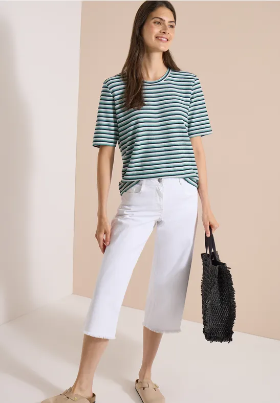 Femme en T-shirt rayé vert, pantalon culotte blanc et sac noir.