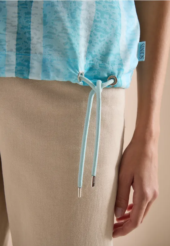 Türkis gestreiftes Top mit Tunnelzug am Saum und Kordeln, kombiniert mit beiger Hose.