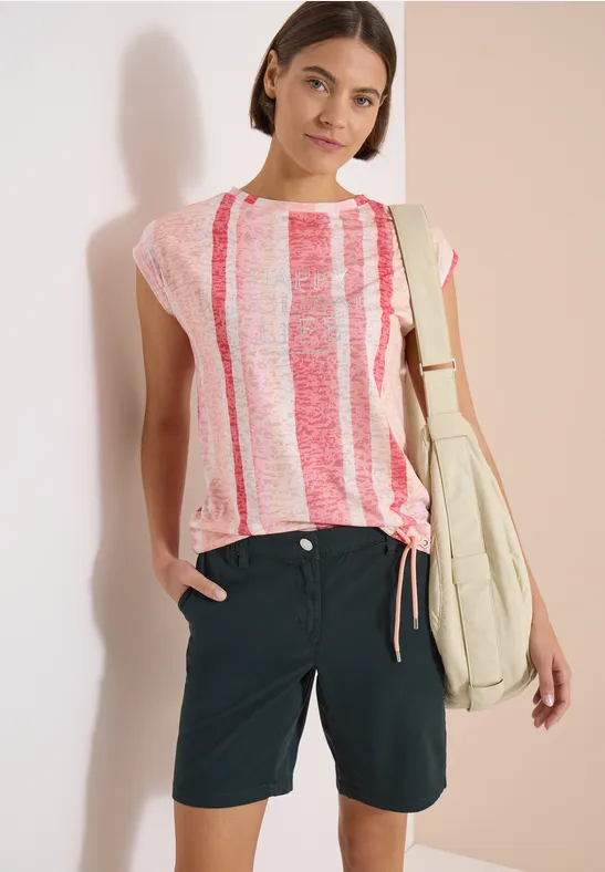 Frau in rosé-weiß gestreiftem T-Shirt, dunkelblauen Shorts und Schultertasche.