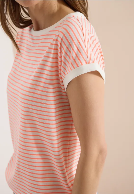 Une personne porte un t-shirt blanc à manches courtes avec de fines rayures horizontales corail sur fond beige.